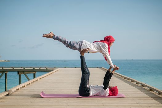 A couple performing acro yoga on a boardwalk by the ocean under a clear sky.