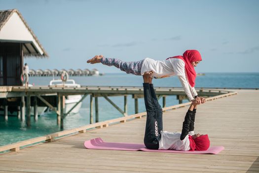 A couple in colorful attire performing acro yoga on a wooden deck by the sea, showcasing balance and harmony.