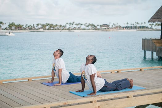 Two men practicing yoga on a deck overlooking the ocean on a sunny day.
