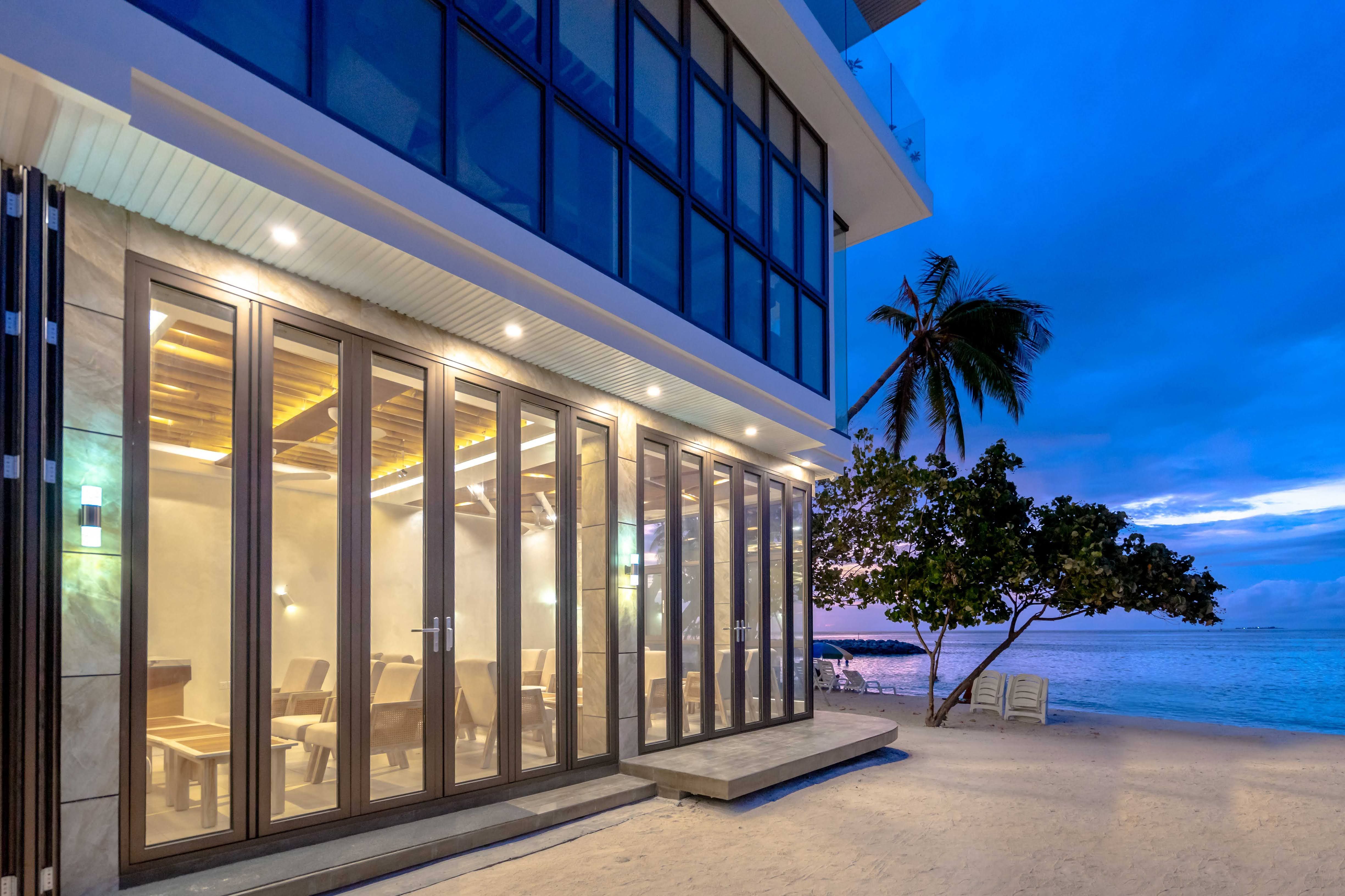A modern glass-fronted building by the beach at twilight, reflecting the serene coastal atmosphere.