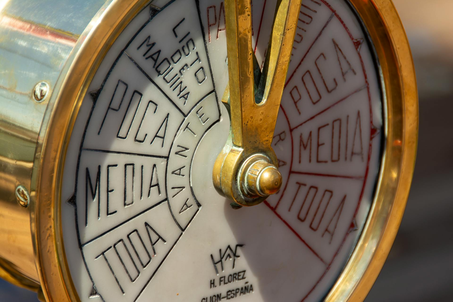 Detailed view of a vintage ship's telegraph dial with Spanish text in sunlight.