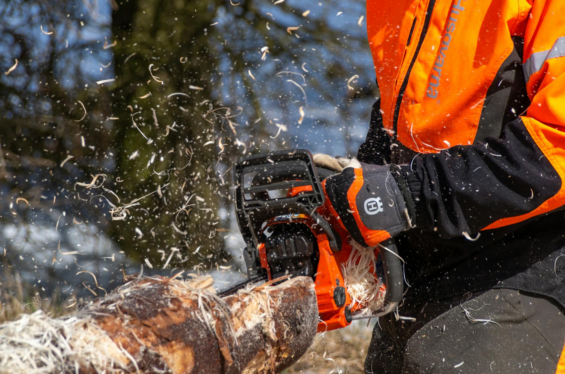 Close-up action shot of a logger using a chainsaw to cut wood outdoors.