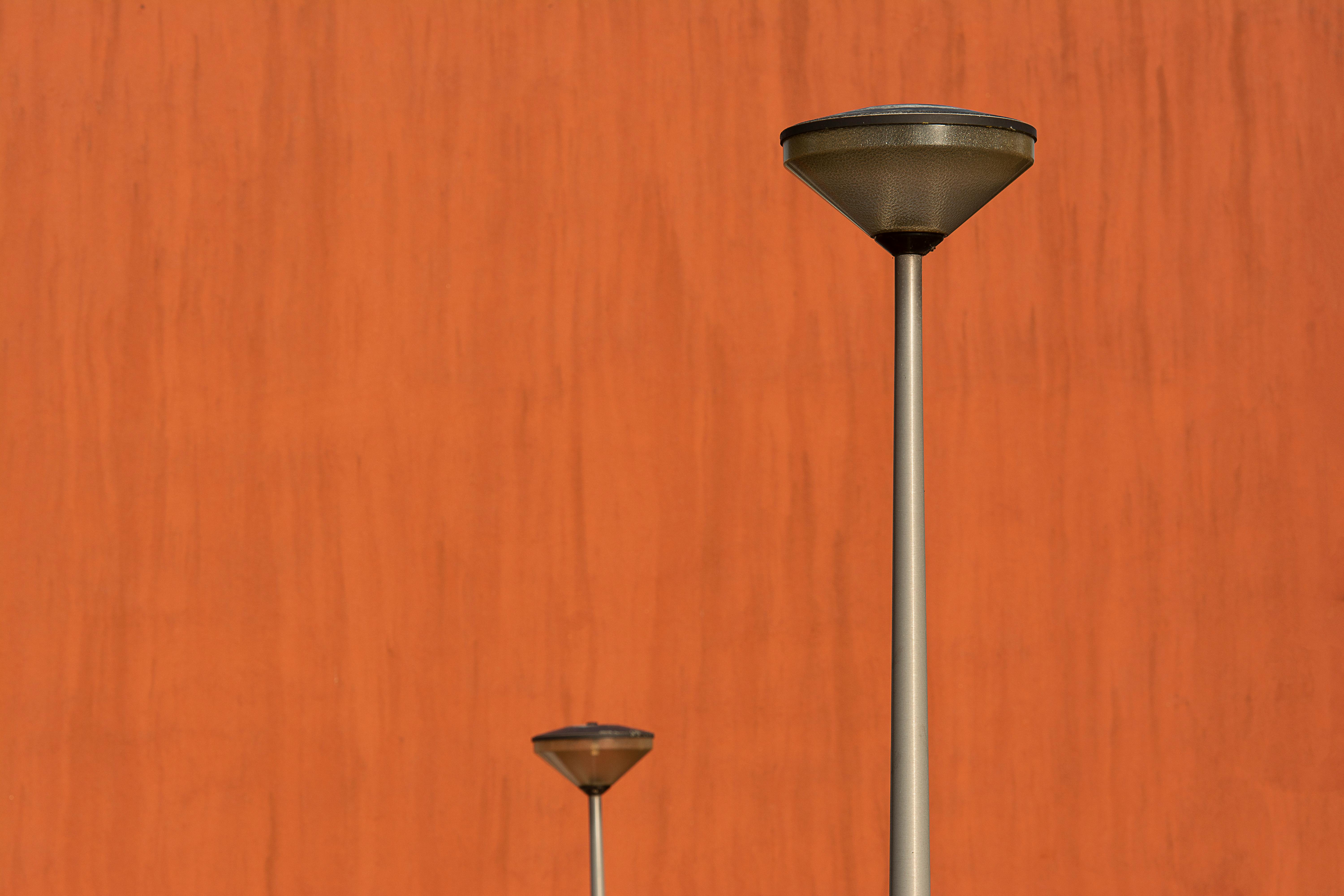 bezplatná Dvě moderní pouliční lampy proti zářivě oranžové texturované zdi v minimalistickém prostředí. Základová fotografie