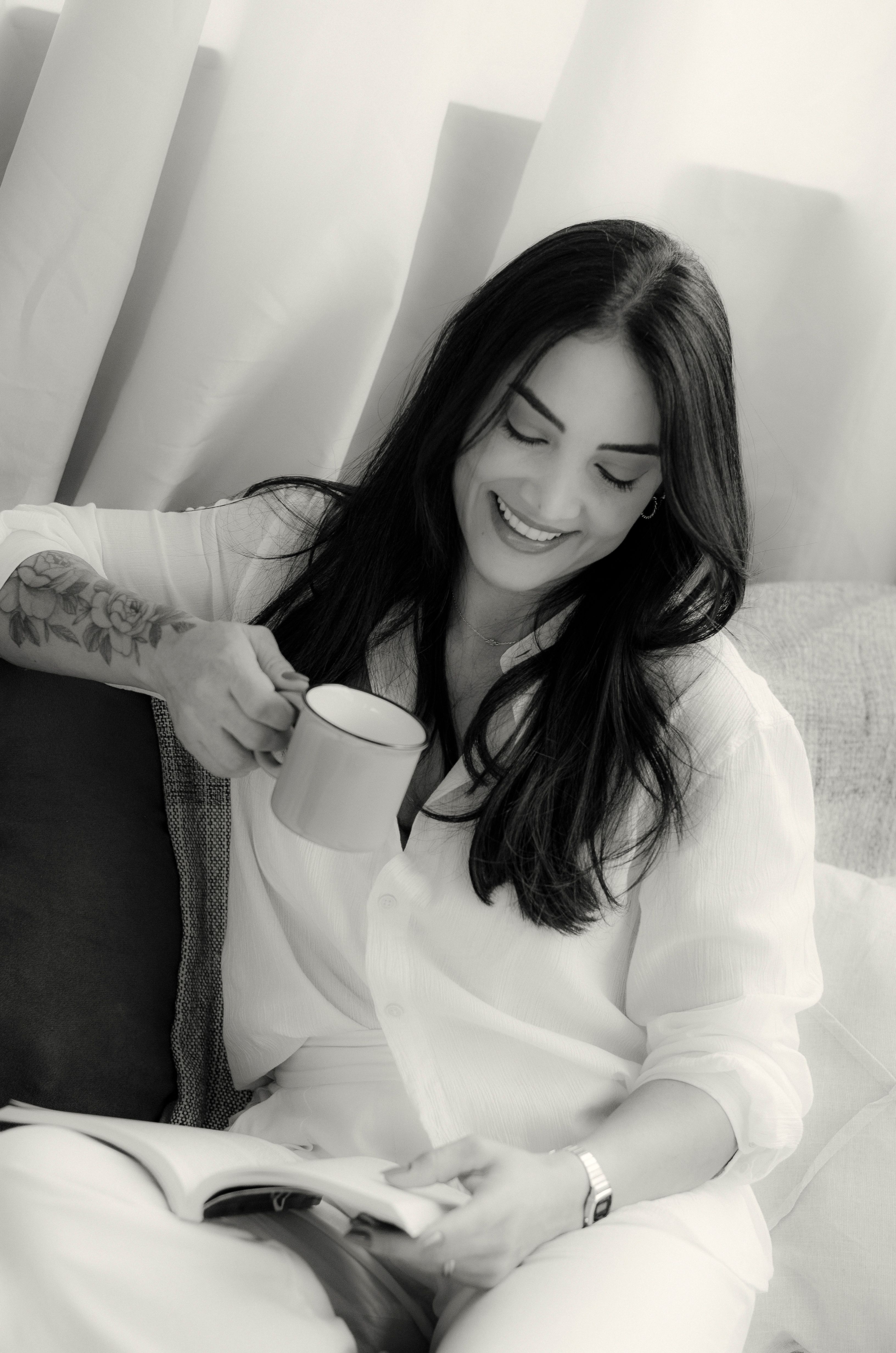 Smiling woman enjoying a coffee while reading indoors, in a cozy setting.