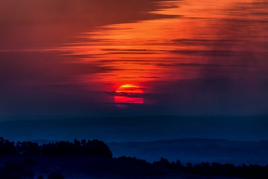 Breathtaking sunset with vivid red and orange hues casting light over a misty landscape.