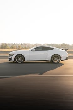 A striking white sports car driving on an open highway under the golden sunrise light.