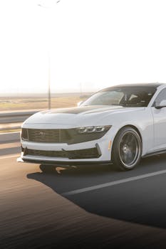 White Ford Mustang in motion on an open road during sunset, showcasing sleek design and performance.