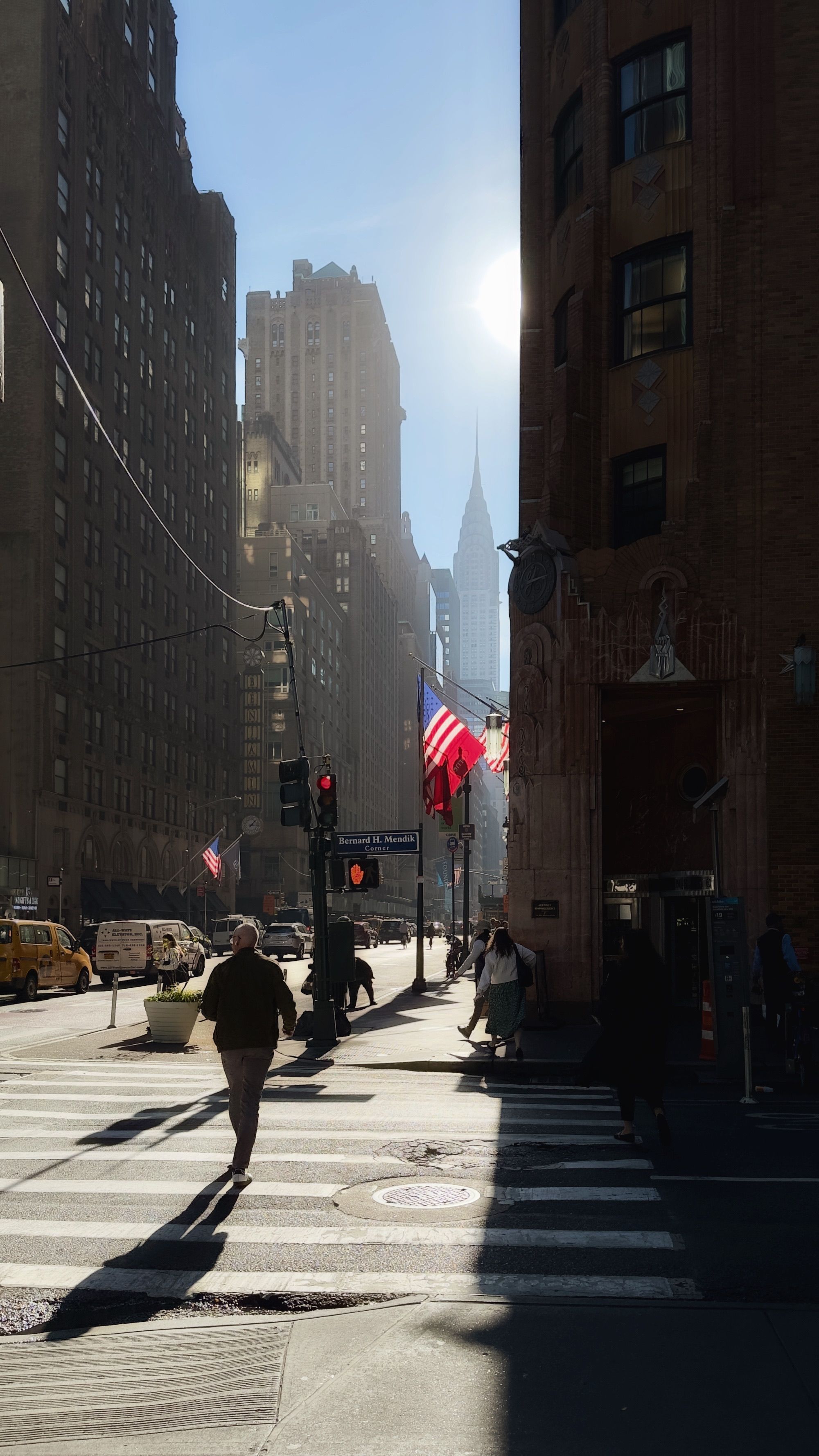 Sunlit New York City street with people walking and American flags flying.