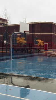 Empty outdoor basketball court in a city setting during a rainy autumn day.