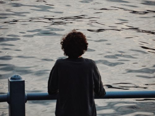 Free A solitary person gazes thoughtfully over calm rippling water, creating a serene and reflective mood. Stock Photo