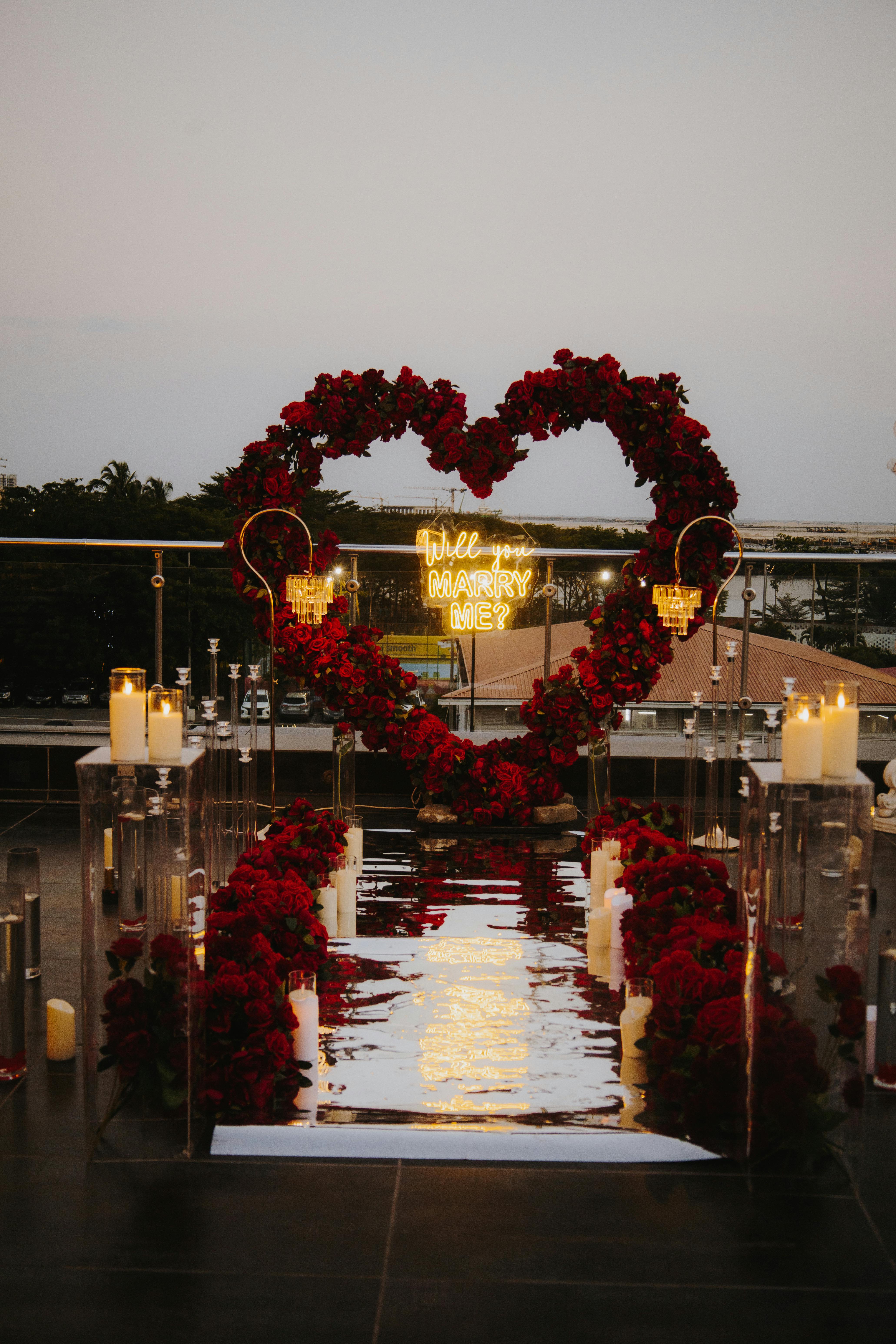 A stunning rooftop proposal setup with a rose heart arch and candles at sunset.