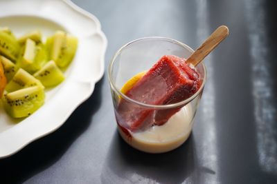 A vibrant berry ice pop in a glass with fresh kiwi on a plate
