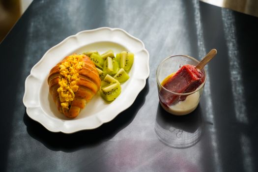 Appetizing breakfast plate with croissant, scrambled eggs, kiwi slices, and a refreshing popsicle.