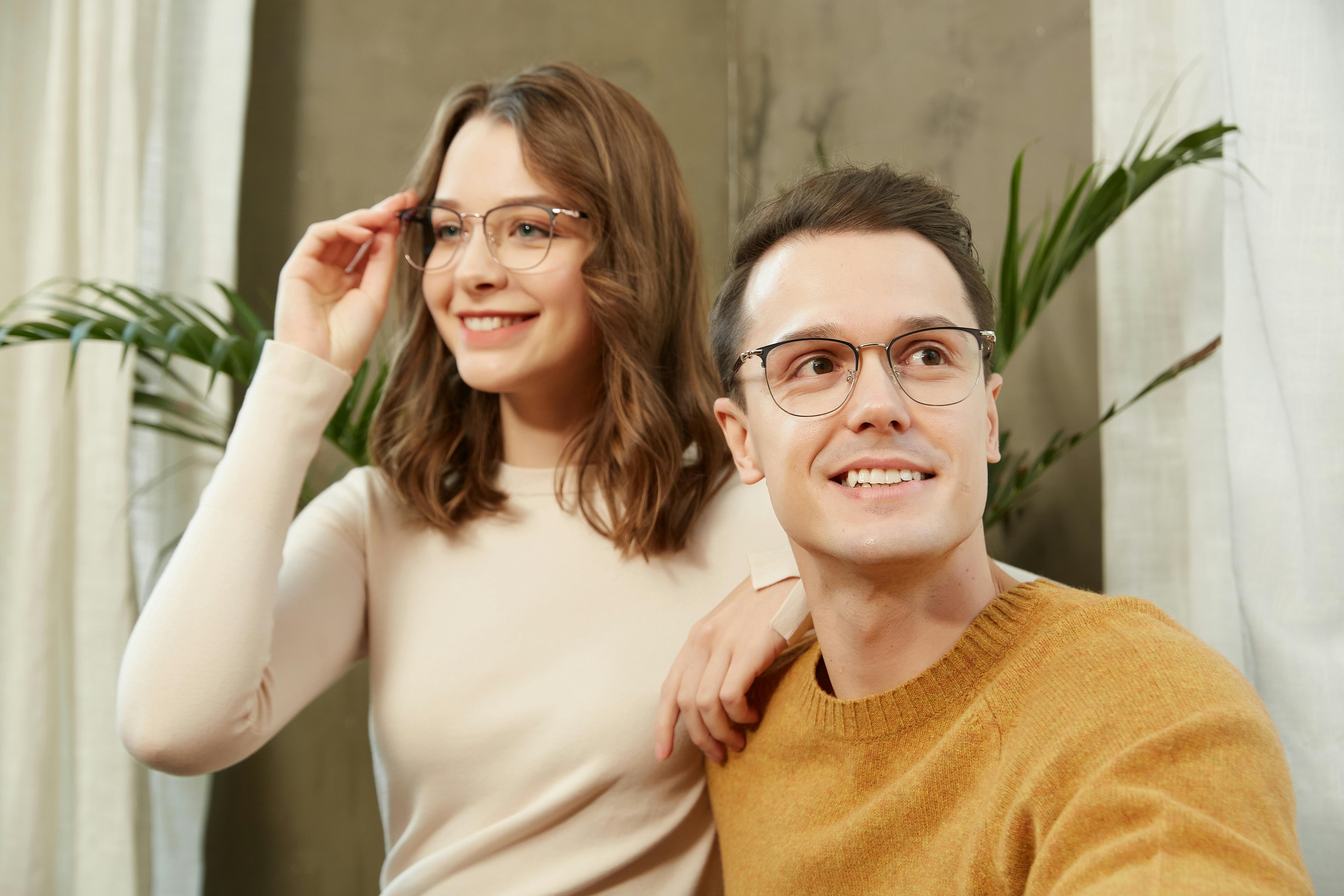 A cheerful couple wearing glasses poses indoors, showcasing modern eyewear fashion.