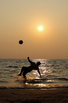 Silhouette of a person playing soccer on Chavakkad Beach at sunset.