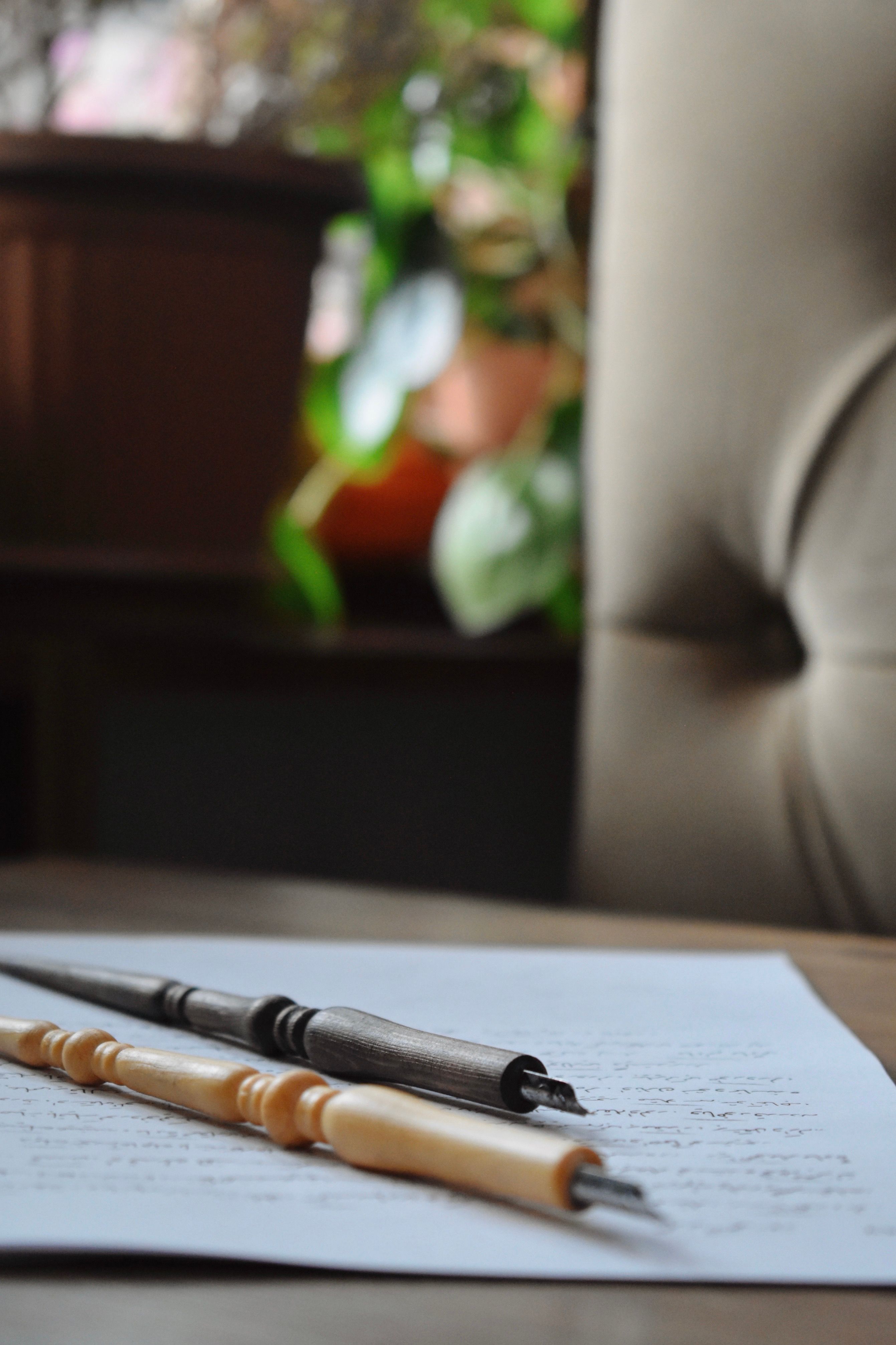 Artistic shot of wooden calligraphy pens resting on handwritten paper indoors.