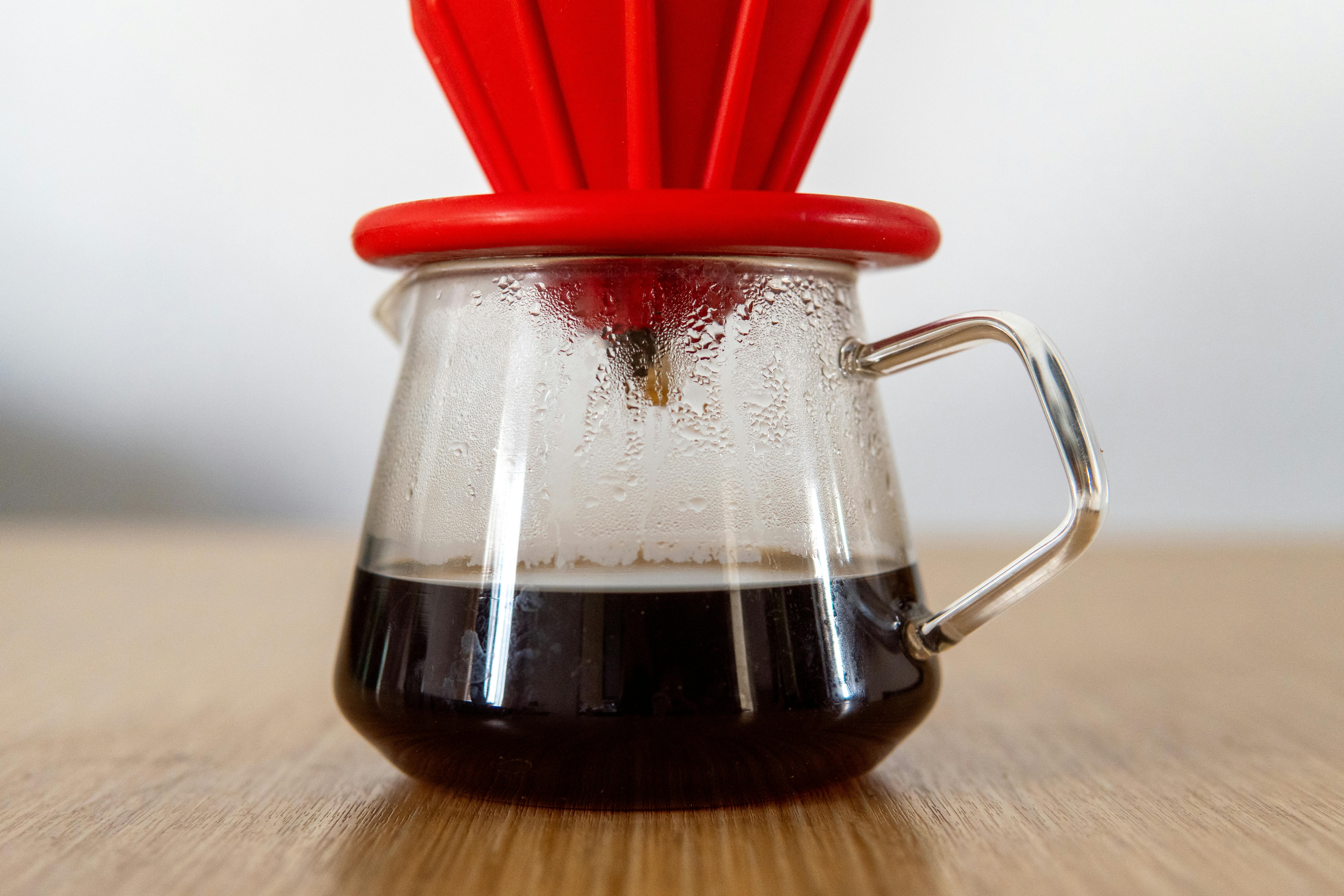 Glass V60 coffee dripper with freshly brewed coffee, showcasing steam and condensation.