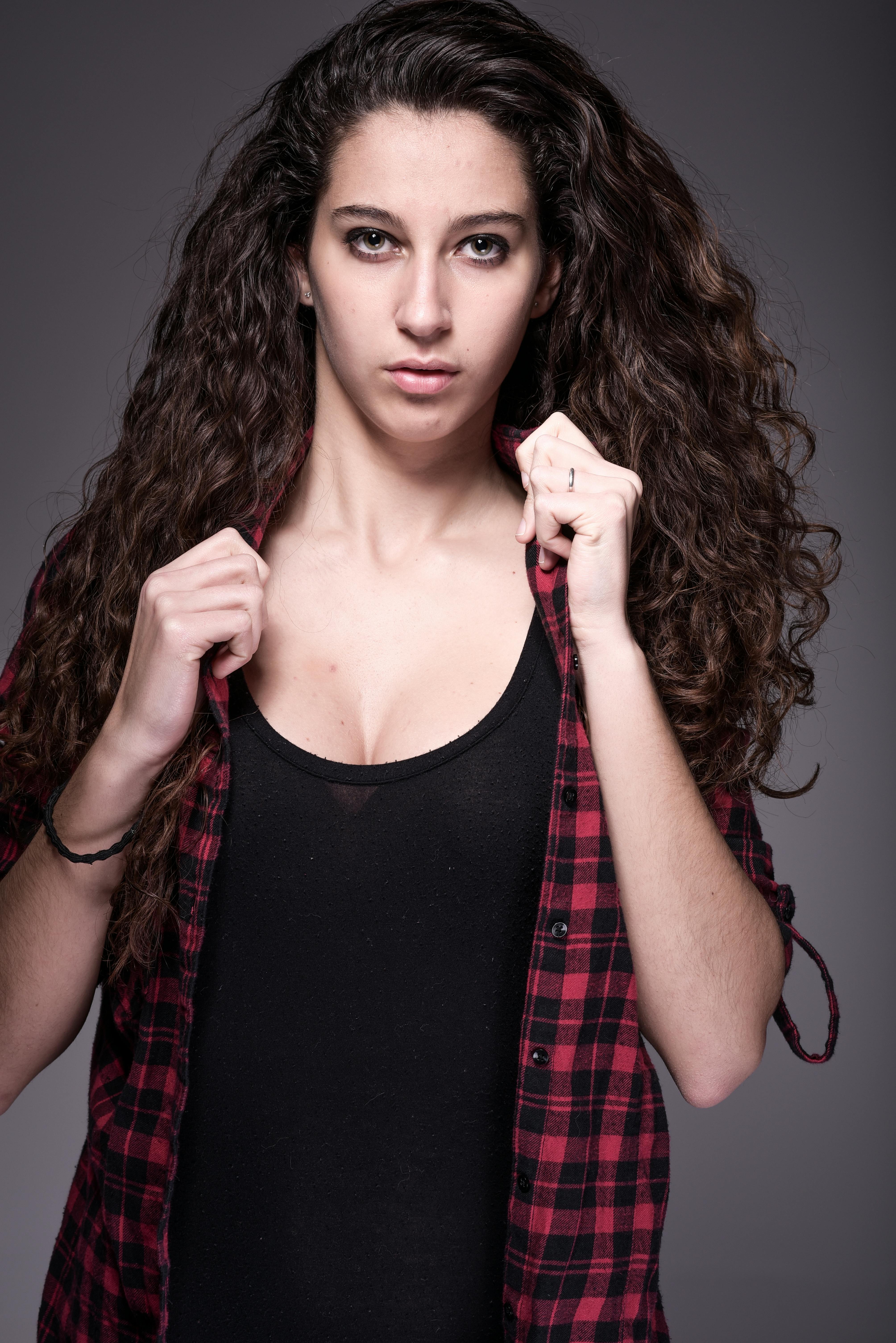A confident woman with curly hair poses in a studio, wearing a plaid shirt.