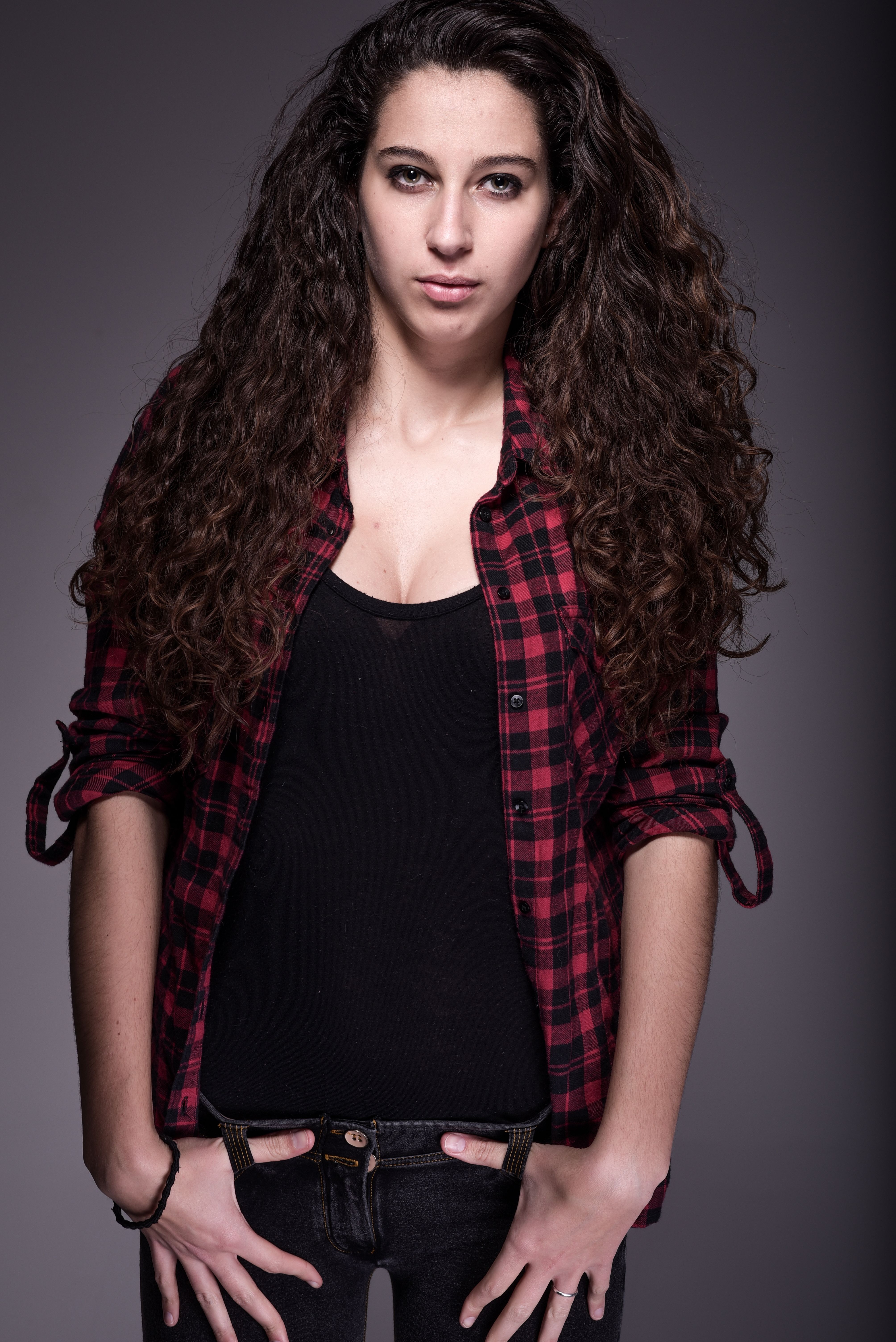 Portrait of a confident woman with long curly hair in a red plaid shirt.