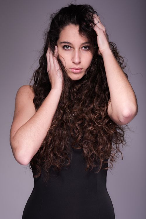 Free Elegant portrait featuring a young woman with long curly hair in a confident pose. Stock Photo