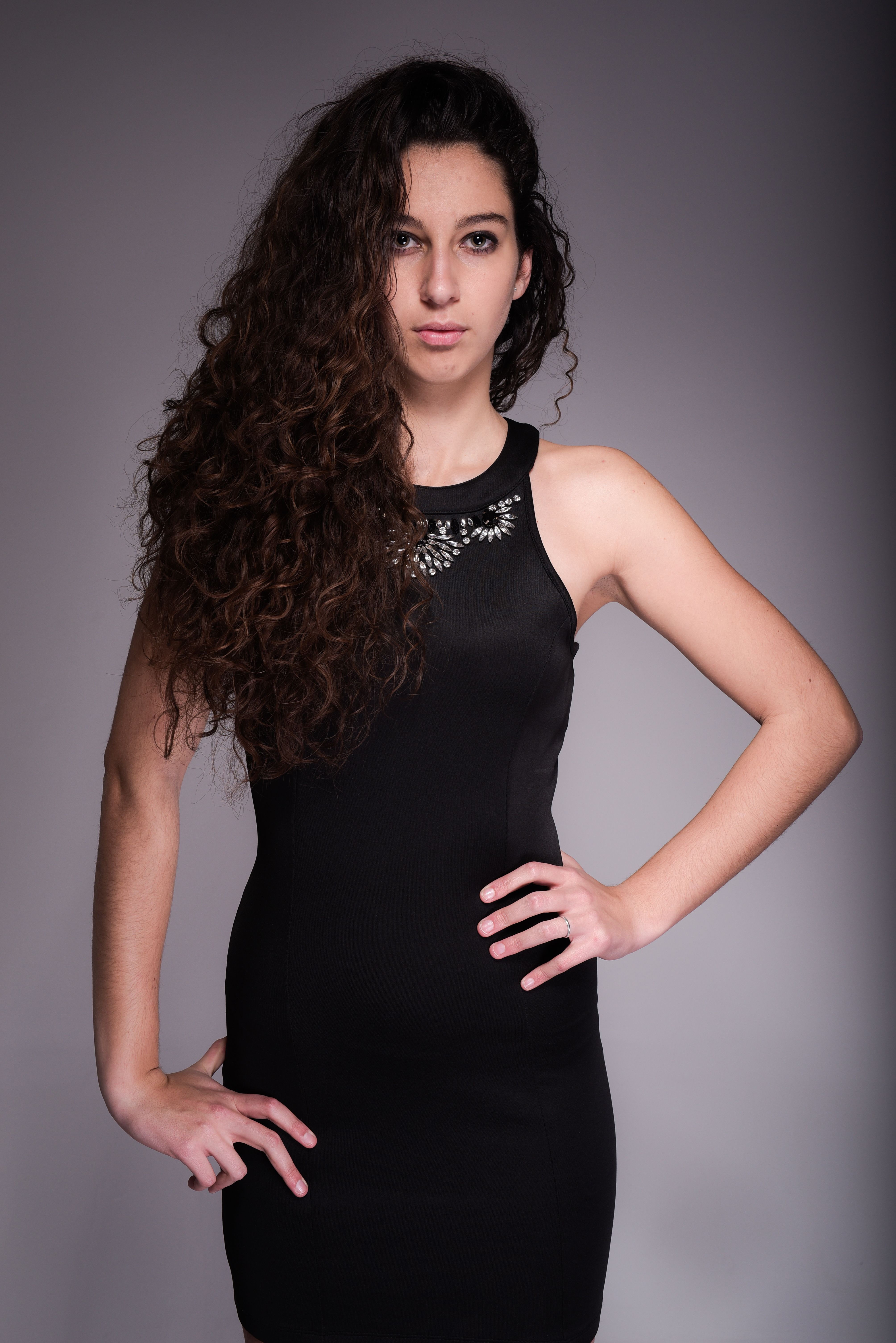 Portrait of a confident woman in black dress with curly hair, studio shot.