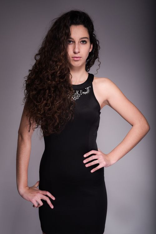 Free Portrait of a confident woman in black dress with curly hair, studio shot. Stock Photo