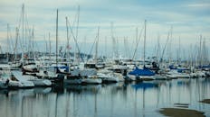 宁静的码头上停靠着各式游艇和帆船，倒映在天空下平静的水面中