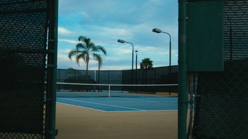 Free Serene view of an empty outdoor tennis court surrounded by palm trees during the day. Stock Photo