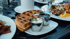 白色盘子上，华夫饼配着糖浆和黄油的特写镜头，呈现出一份完美的早餐布置