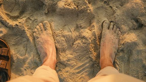 Free Top view of bare feet on a sandy beach, capturing a relaxed travel moment at sunset. Stock Photo