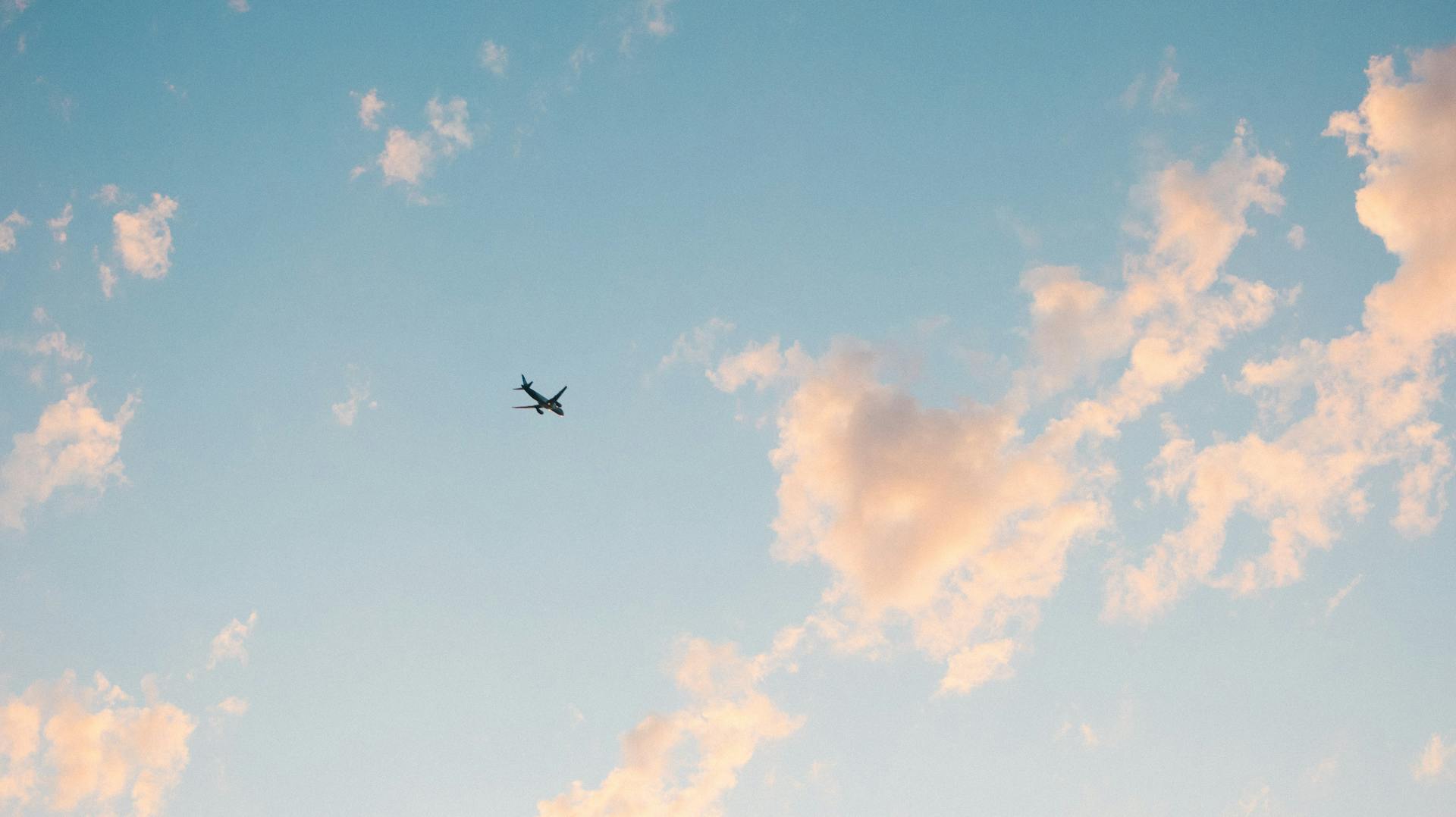 A lone airplane soars through a beautiful blue sky with scattered clouds, illustrating air travel.