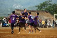 Football players celebrating a goal in a dusty outdoor match with spectators.