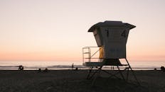 日落时分，海滩景色宁静，救生塔和人们的剪影清晰可见