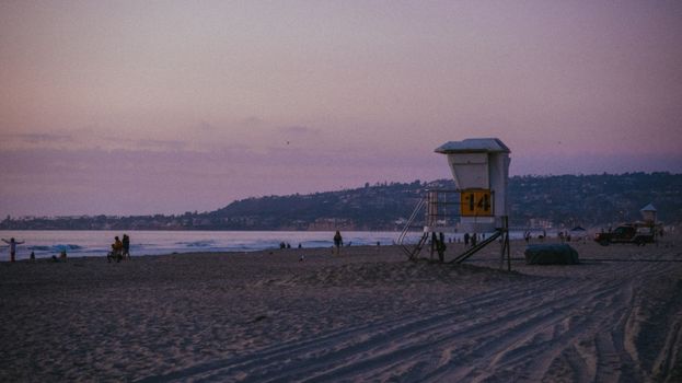 Serene beach at sunset with a lifeguard tower and silhouettes of people enjoying the shore.