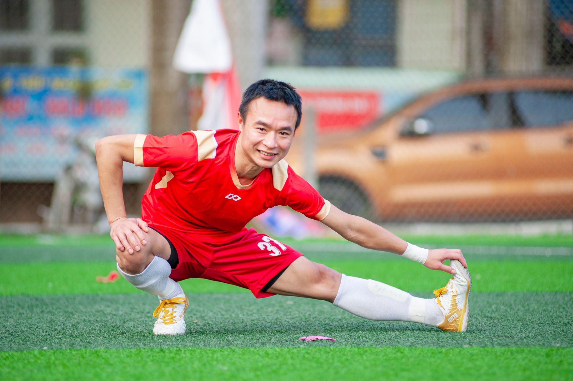 Athlete in red jersey stretching on lush green field in Hanoi, Vietnam.
