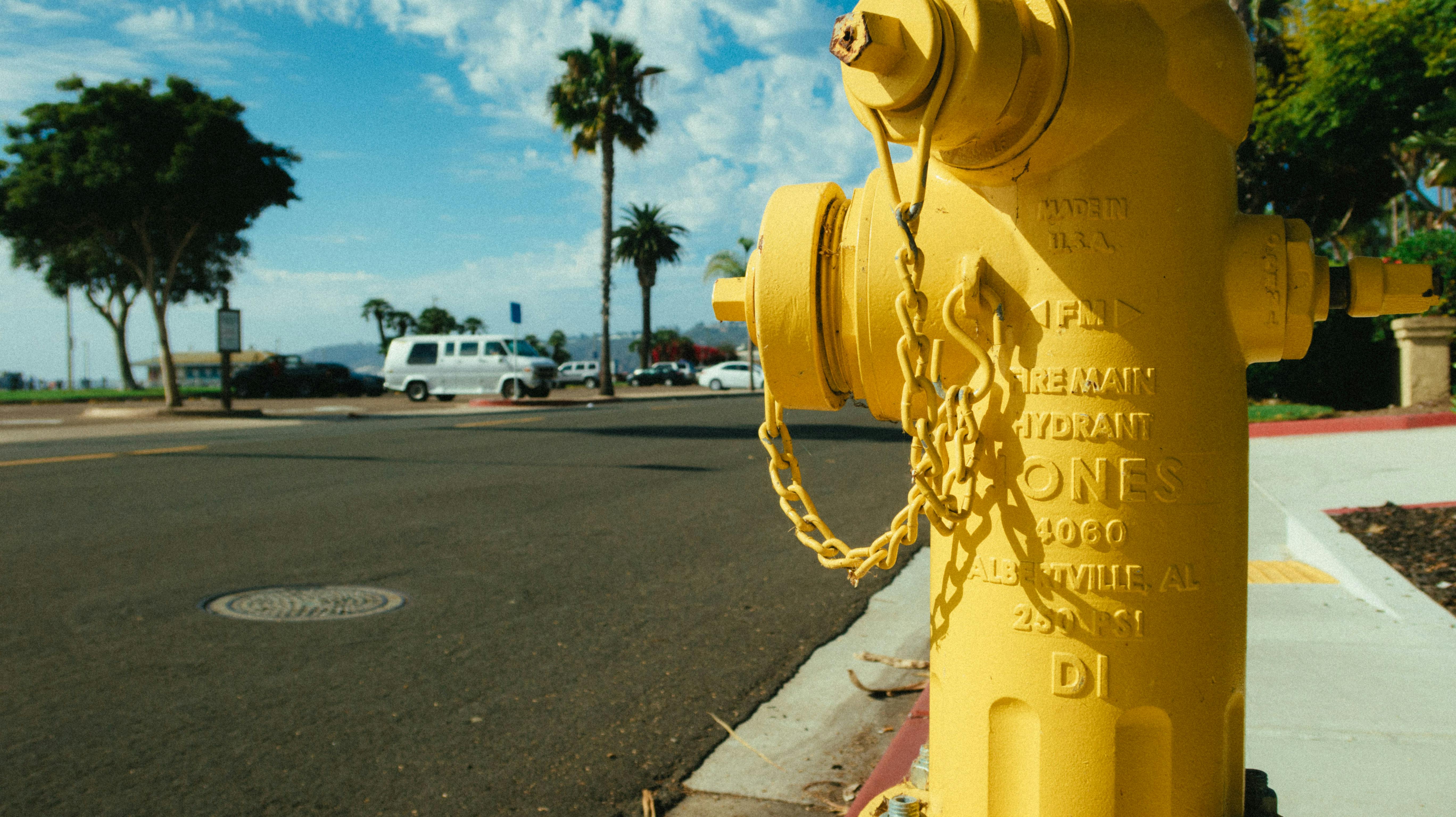 Vibrant yellow fire hydrant in a sunny urban street setting with palm trees.