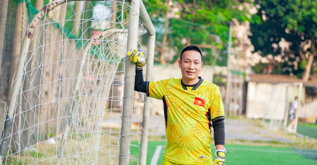 Vietnamese soccer player in a yellow goalkeeper uniform posing by a goal on a sunny day.