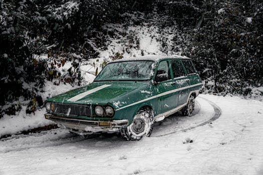 A vintage green car parked on a snowy forest road, surrounded by winter scenery.