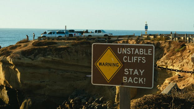 悬崖边立着警告标志，附近停着车，背景是海