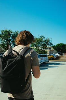 夏天，一名男子背着背包，走过阳光明媚的停车场