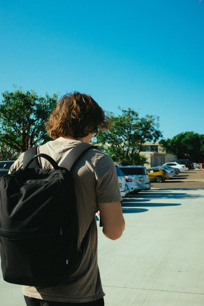 Someone crossing a sunlit yard with a soft-shell pack on one shoulder — photo by Athena Sandrini on Pexels