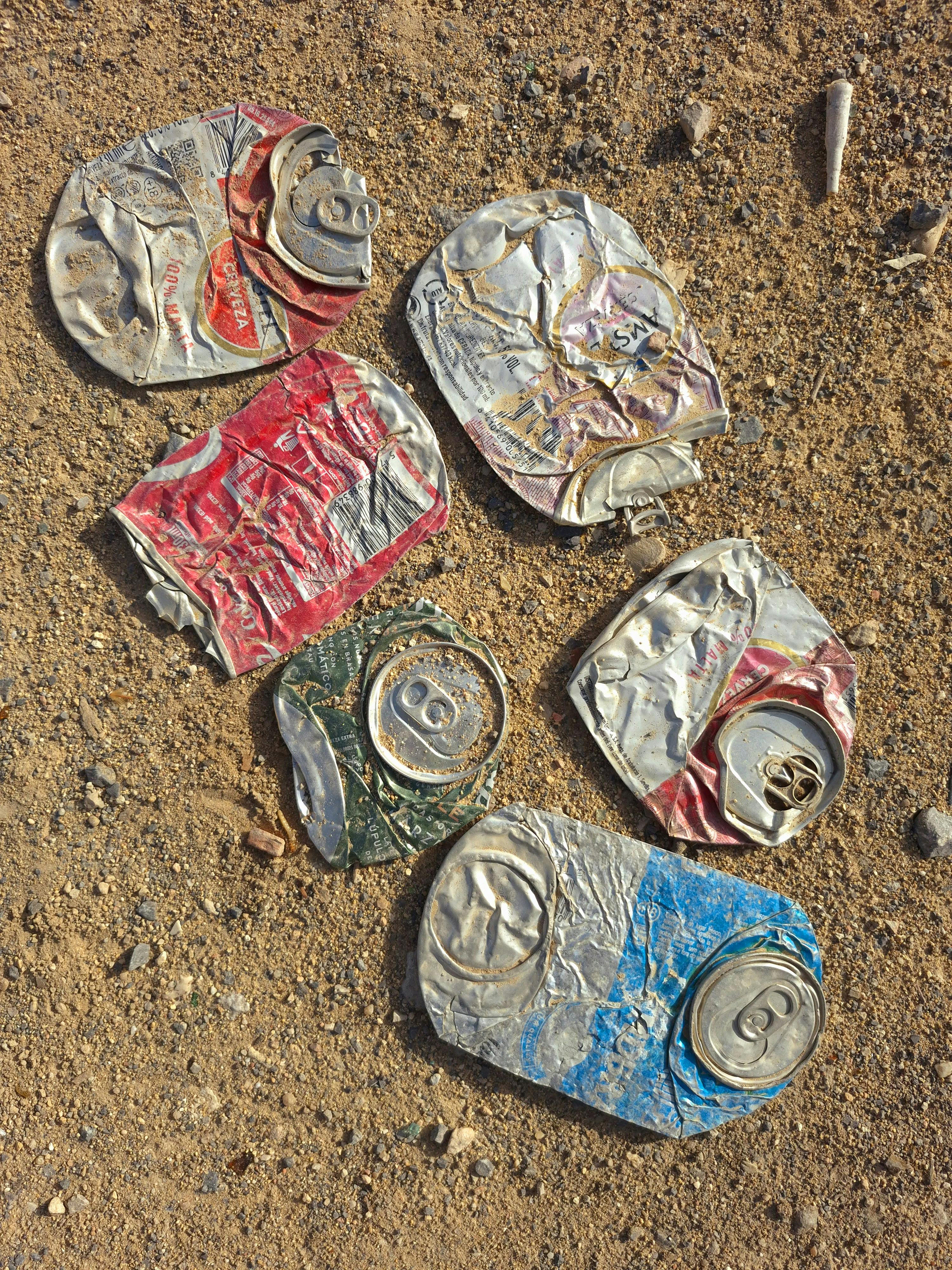 Close-up of six crushed beverage cans on sandy ground, conveying recycling symbolism.