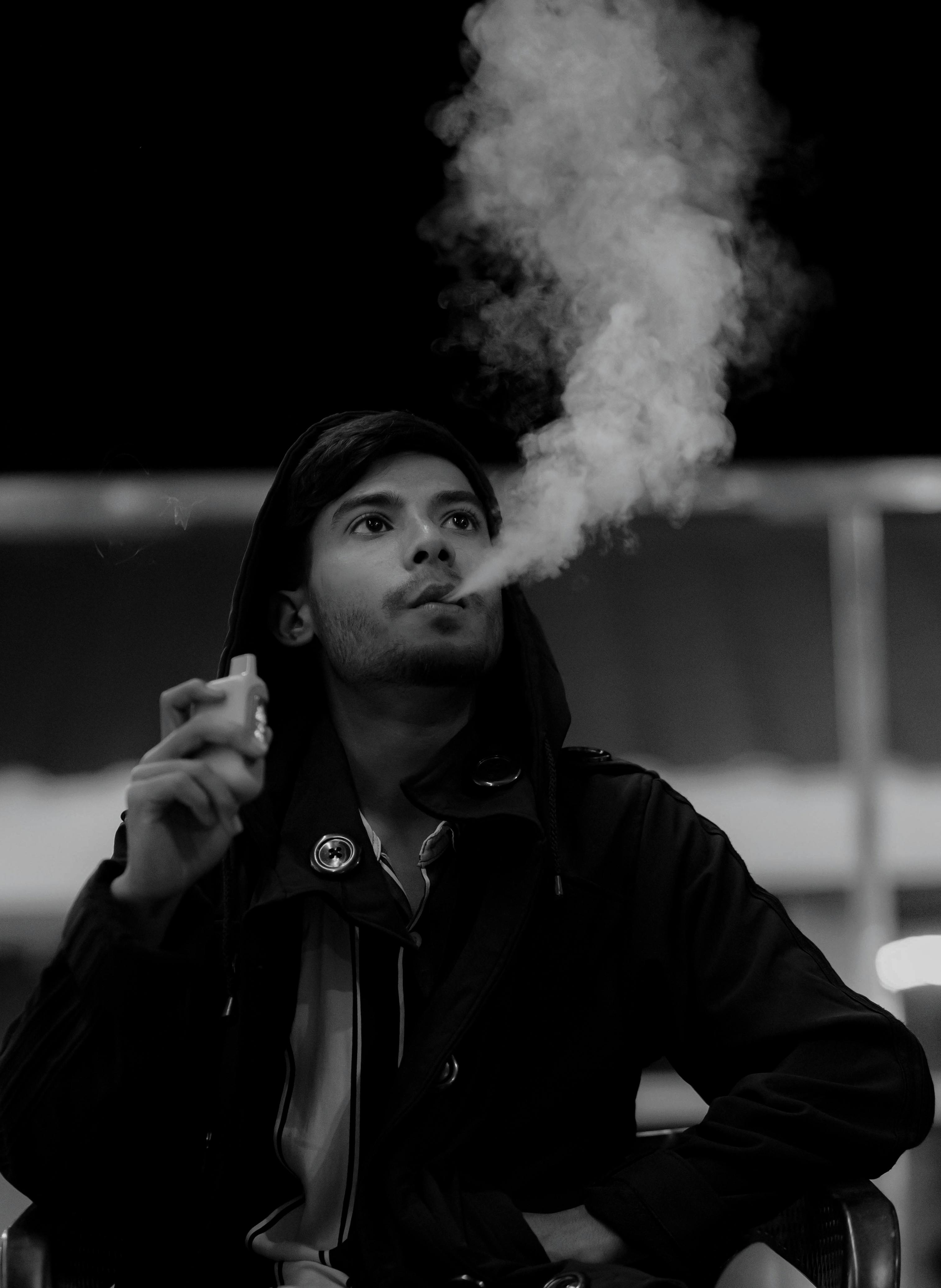 young man vaping at night in black and white