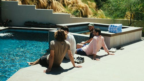 四名男子坐在游泳池旁邊