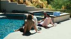 一群朋友在阳光明媚的泳池边放松交谈，享受着户外休闲时光