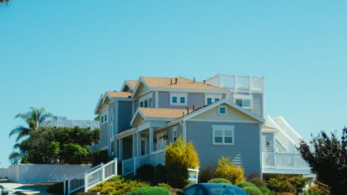 Free Bright suburban home with garden on a sunny day, featuring blue sky and greenery. Stock Photo