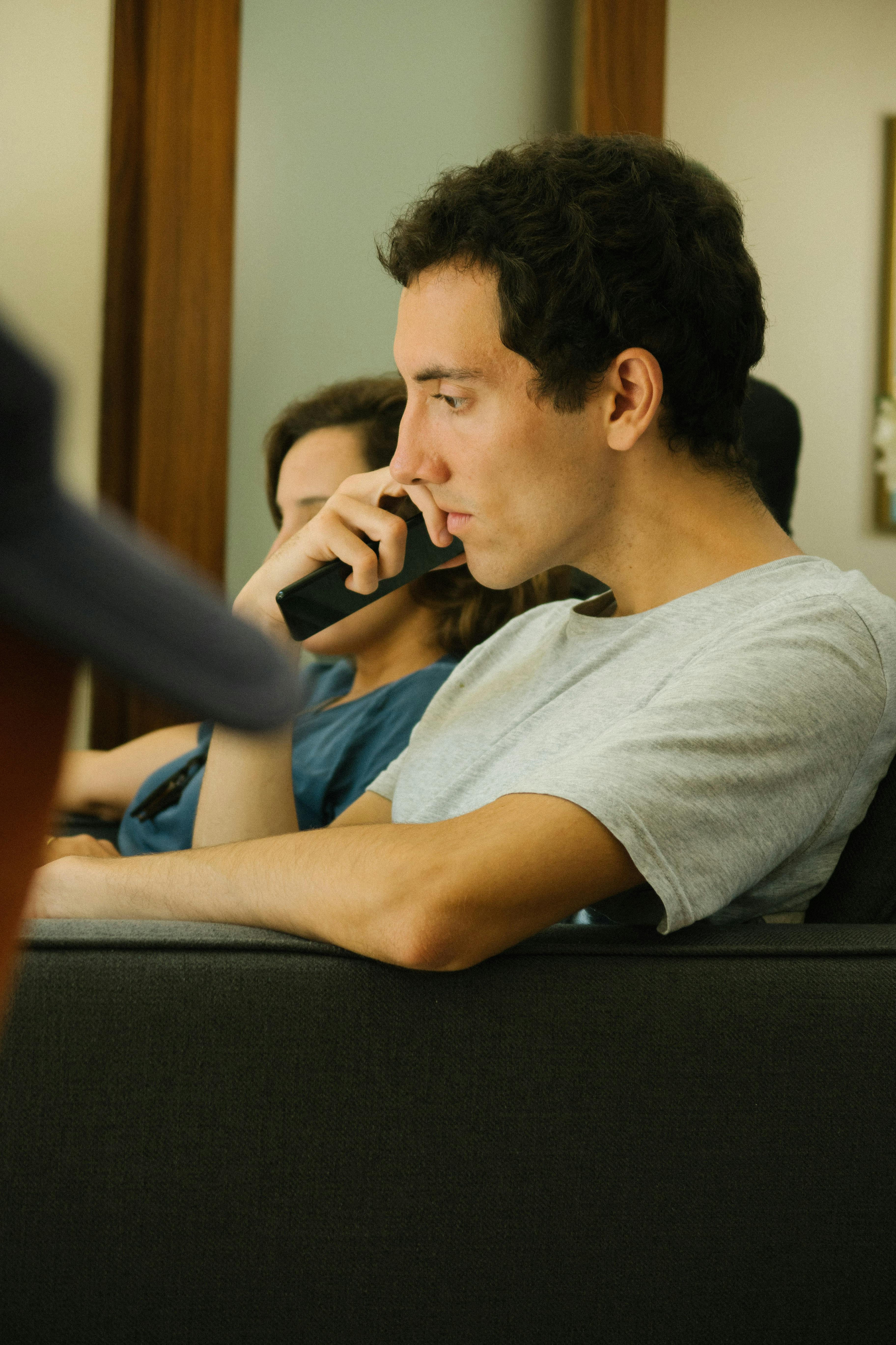 年轻人若有所思地托着下巴，坐在室内的沙发上