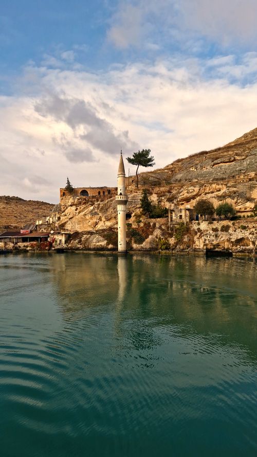 Free Scenic waterside view with a mosque against rocky hills under dramatic sky. Tranquil atmosphere. Stock Photo