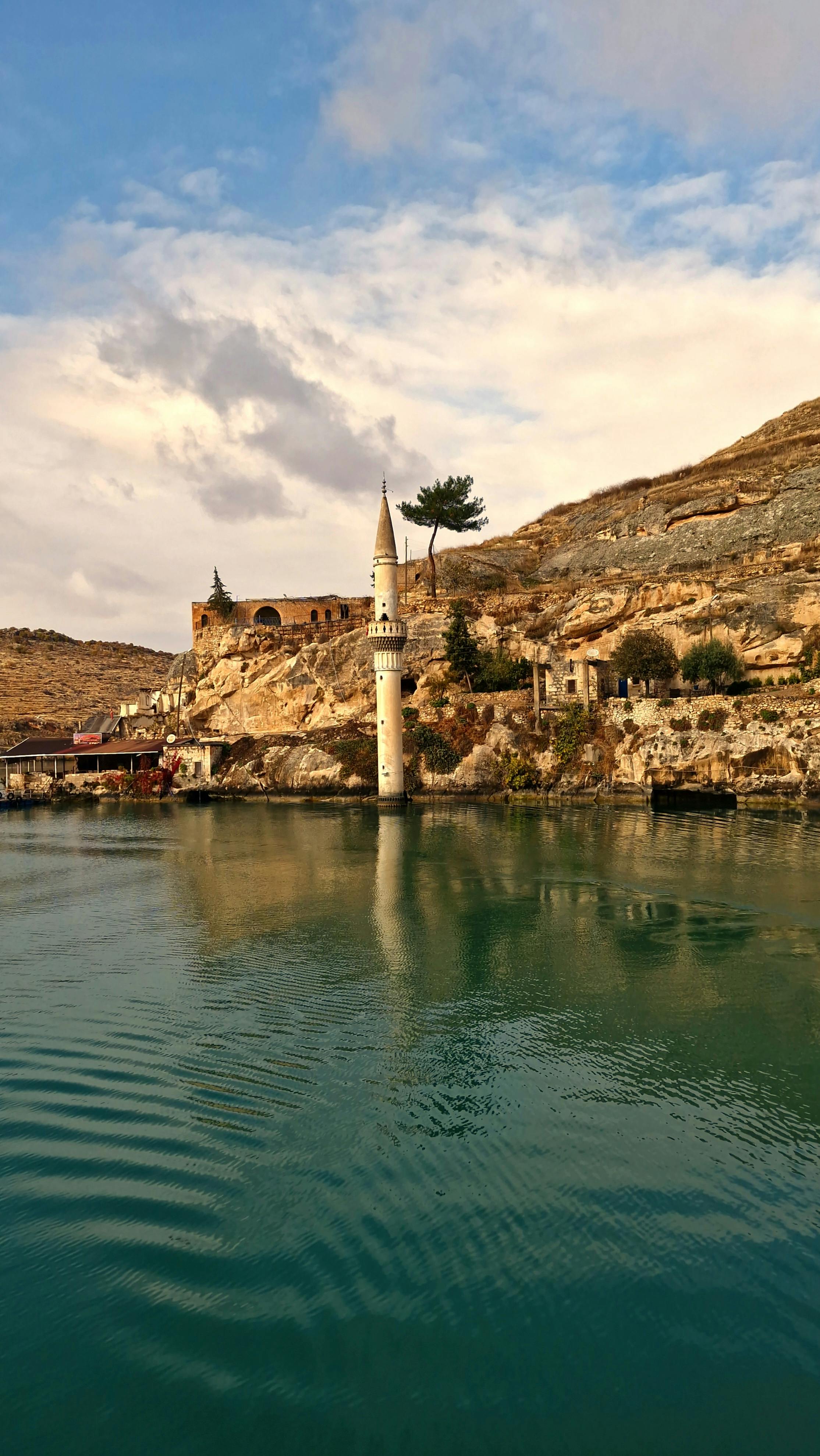 Scenic view of the submerged mosque tower in Halfeti with calm water and rocky landscape.