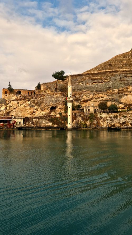 Free Minaret rising from waters, set against ancient rocky cliffs under a cloudy sky. Stock Photo